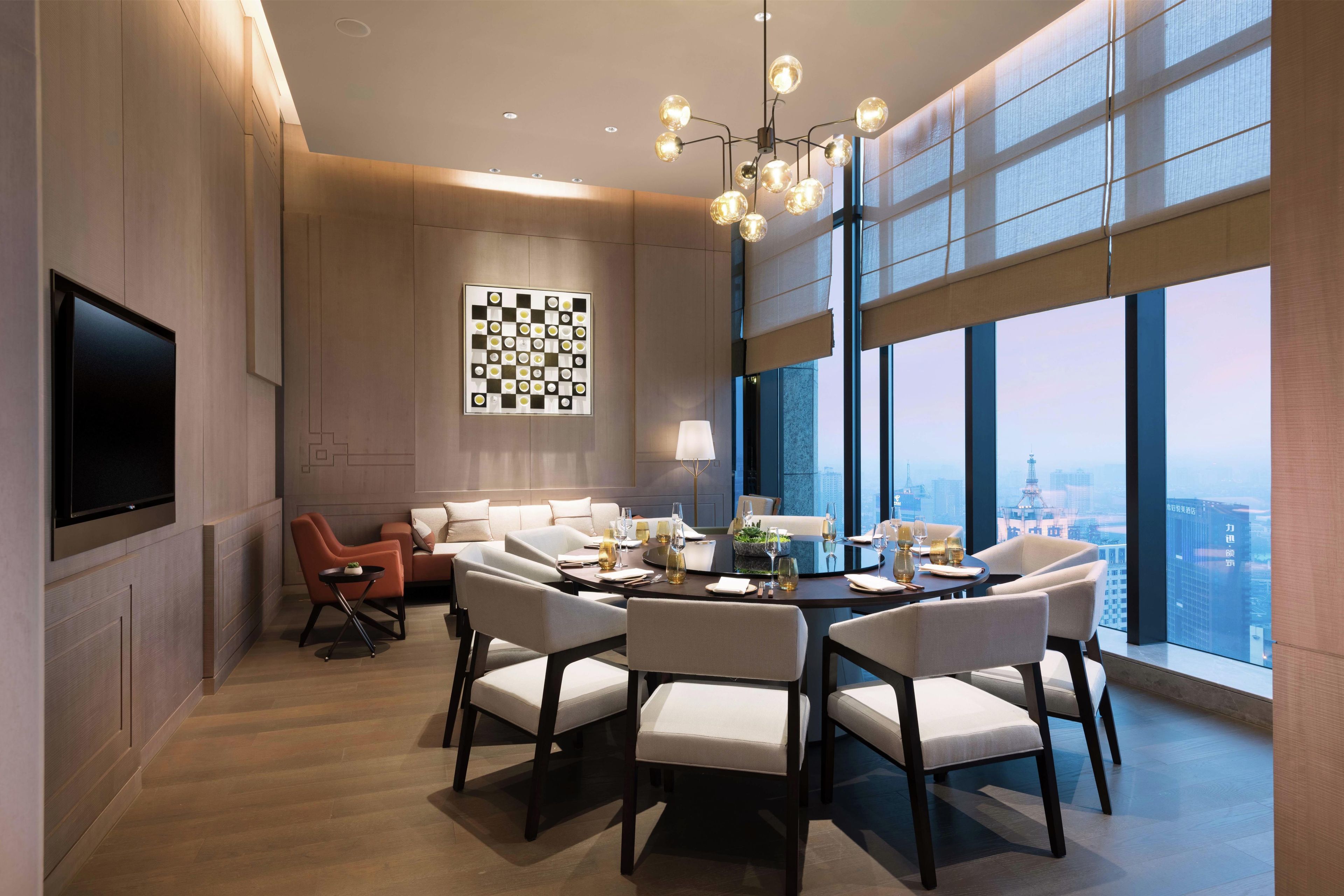 A modern dining area with a round table, chairs, and a city view through large windows.
