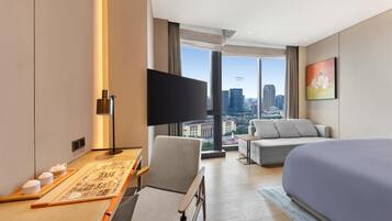 Habitación de hotel con cama, escritorio con televisor de pantalla plana, sofá y ventana grande con vistas a la ciudad.