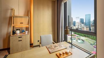A hotel room with a city view, a desk with a laptop, a chair, a small cabinet with a coffee maker, and a window with curtains.