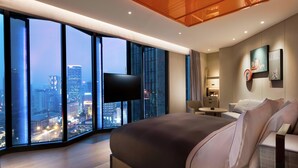 Una habitación de hotel moderna con una cama grande, televisión de pantalla plana, vista a la ciudad y una pequeña zona de estar.