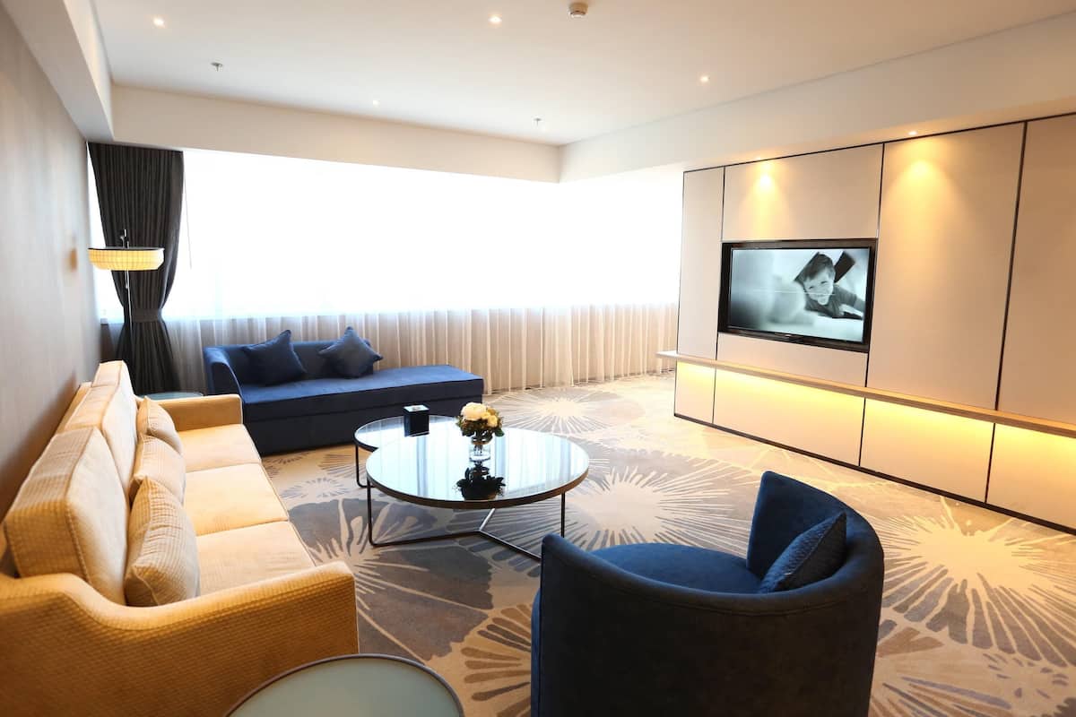 A modern living room with a sofa, armchair, coffee table, and a TV mounted on the wall.