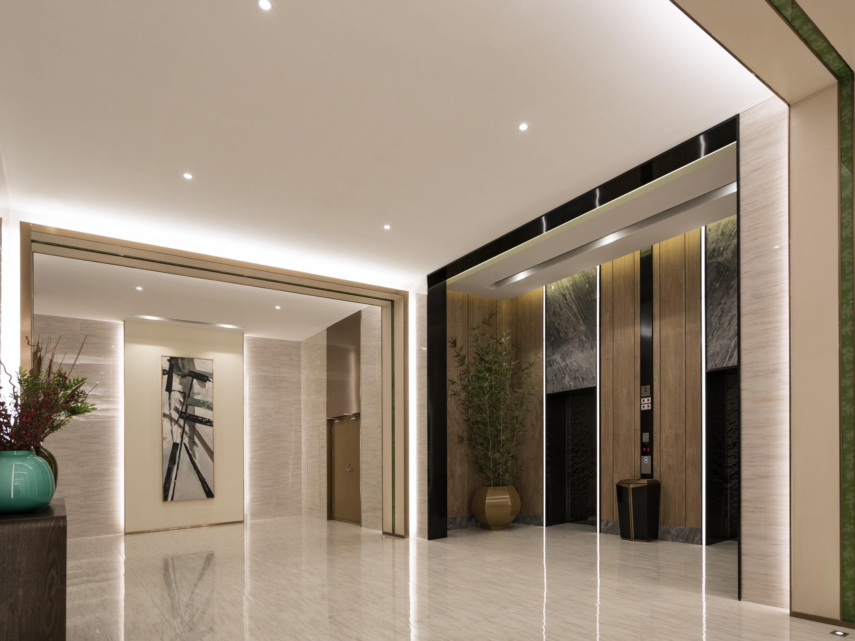 A modern lobby with a polished floor, a large potted plant, a framed artwork, and a reception desk.