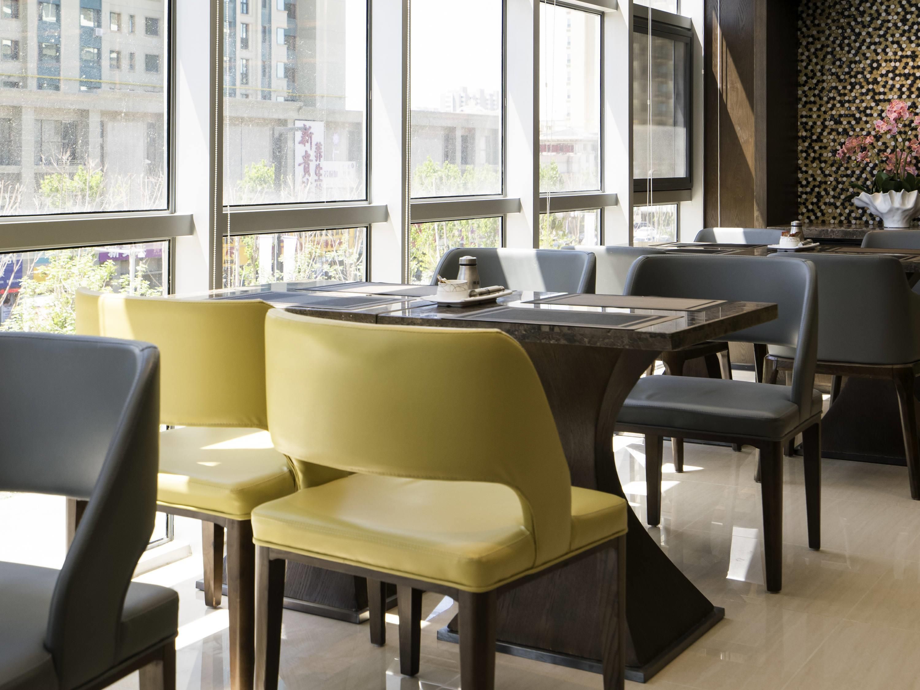 A modern dining area with a large table, yellow and gray chairs, and large windows offering a view of buildings.
