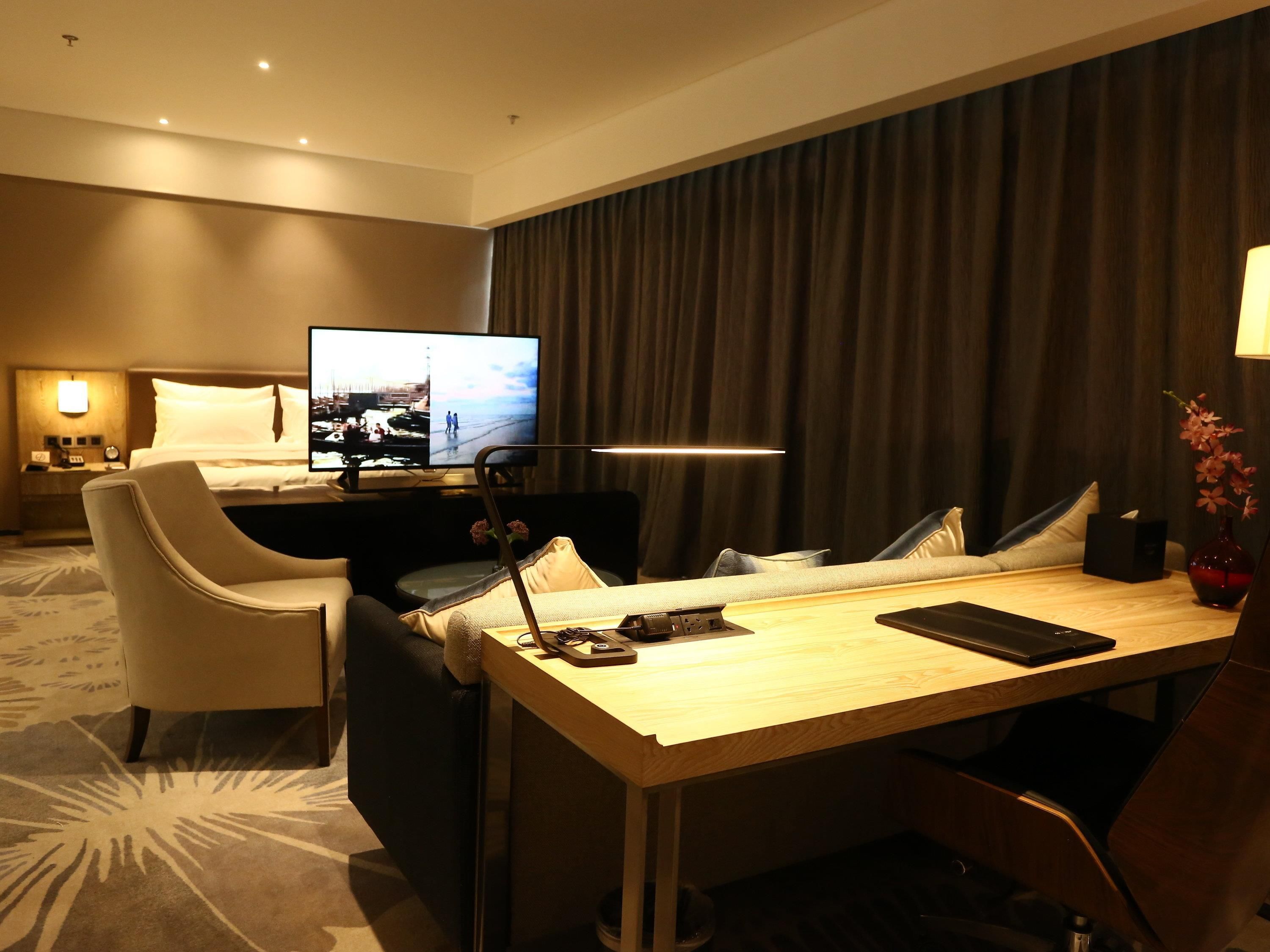 Habitación de hotel con una cama, televisión, escritorio con una computadora portátil, silla y mesa.