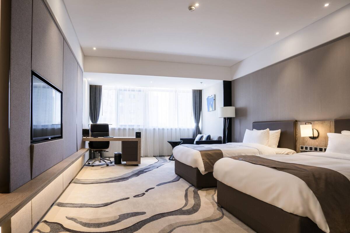 A modern hotel room with a large bed, a desk, a chair, and a TV.