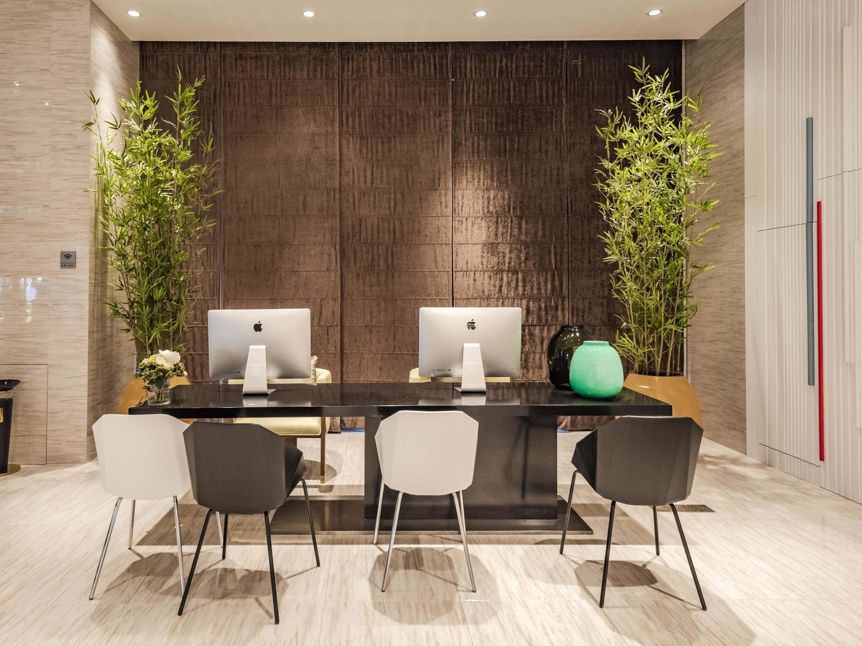 A modern conference room with two Apple iMac computers, a black table, four chairs, and decorative plants.