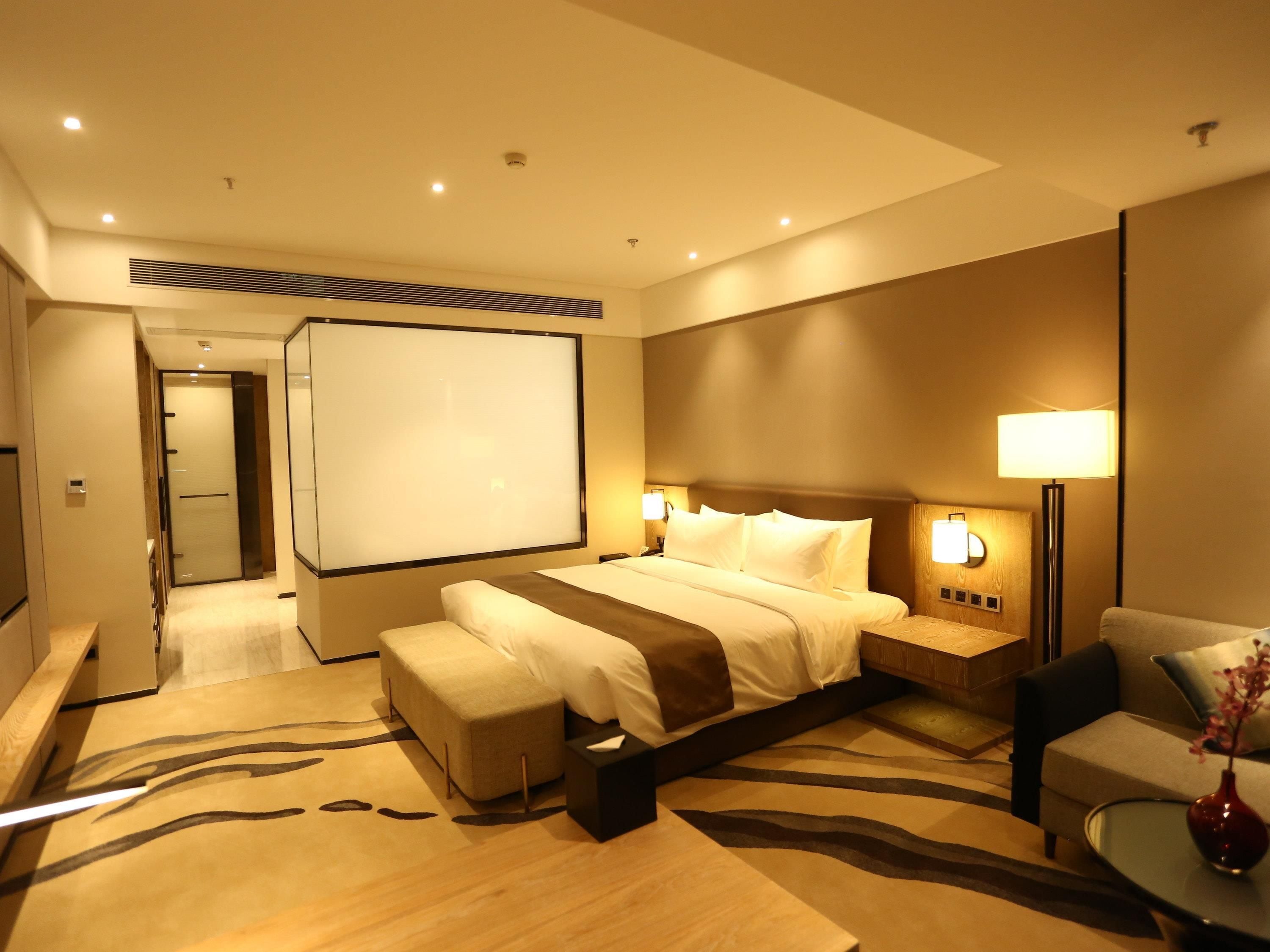A hotel room with a large bed, bedside tables, a seating area, and a projector screen.