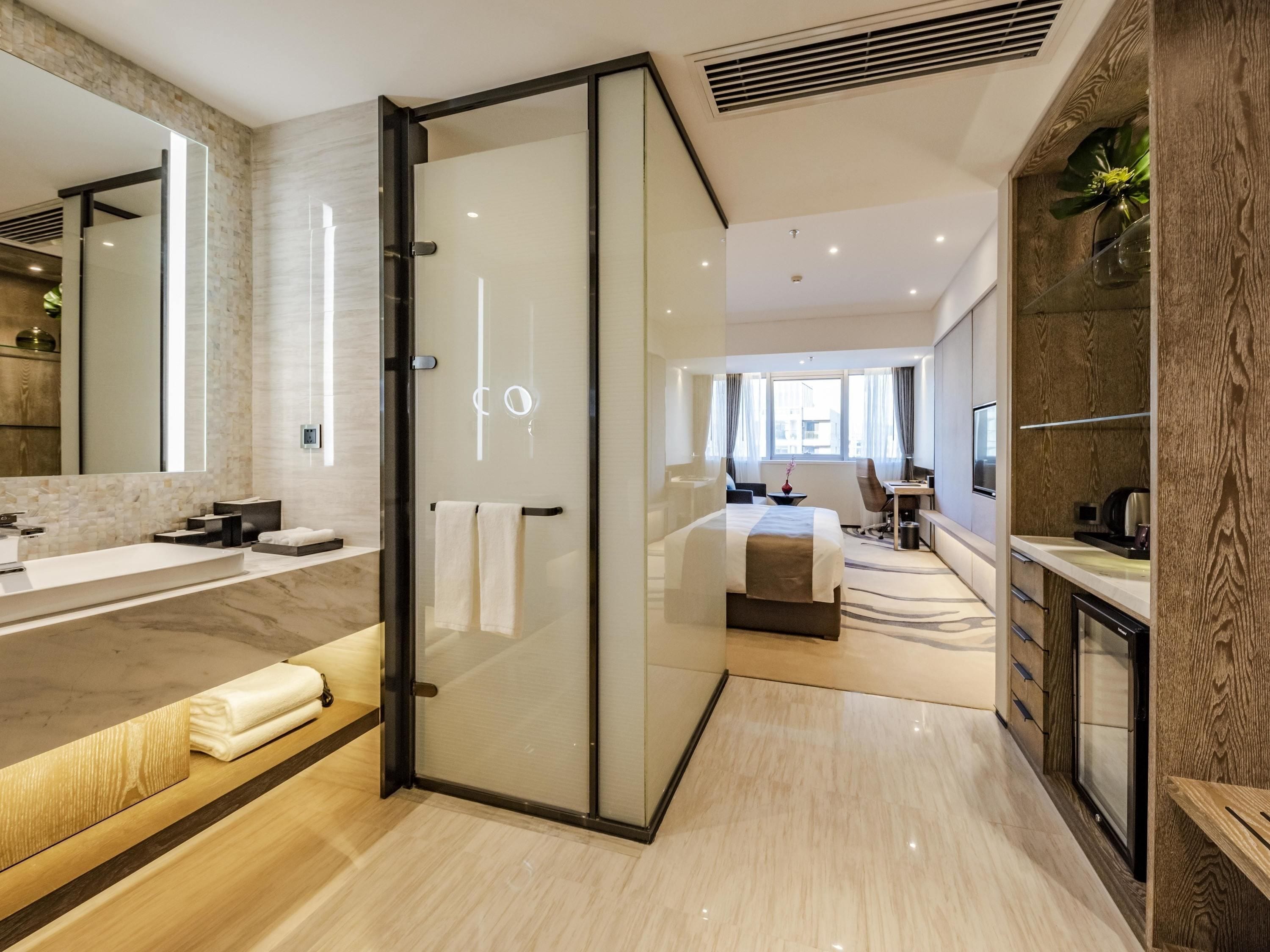 A modern hotel bathroom with a glass shower enclosure, a large mirror, and a vanity with a marble countertop.