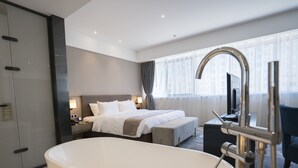 Une chambre d’hôtel moderne dotée d’une grande baignoire, d’un lit parfaitement fait, d’un bureau avec un ordinateur et offrant une vue sur la ville grâce à de grandes fenêtres.