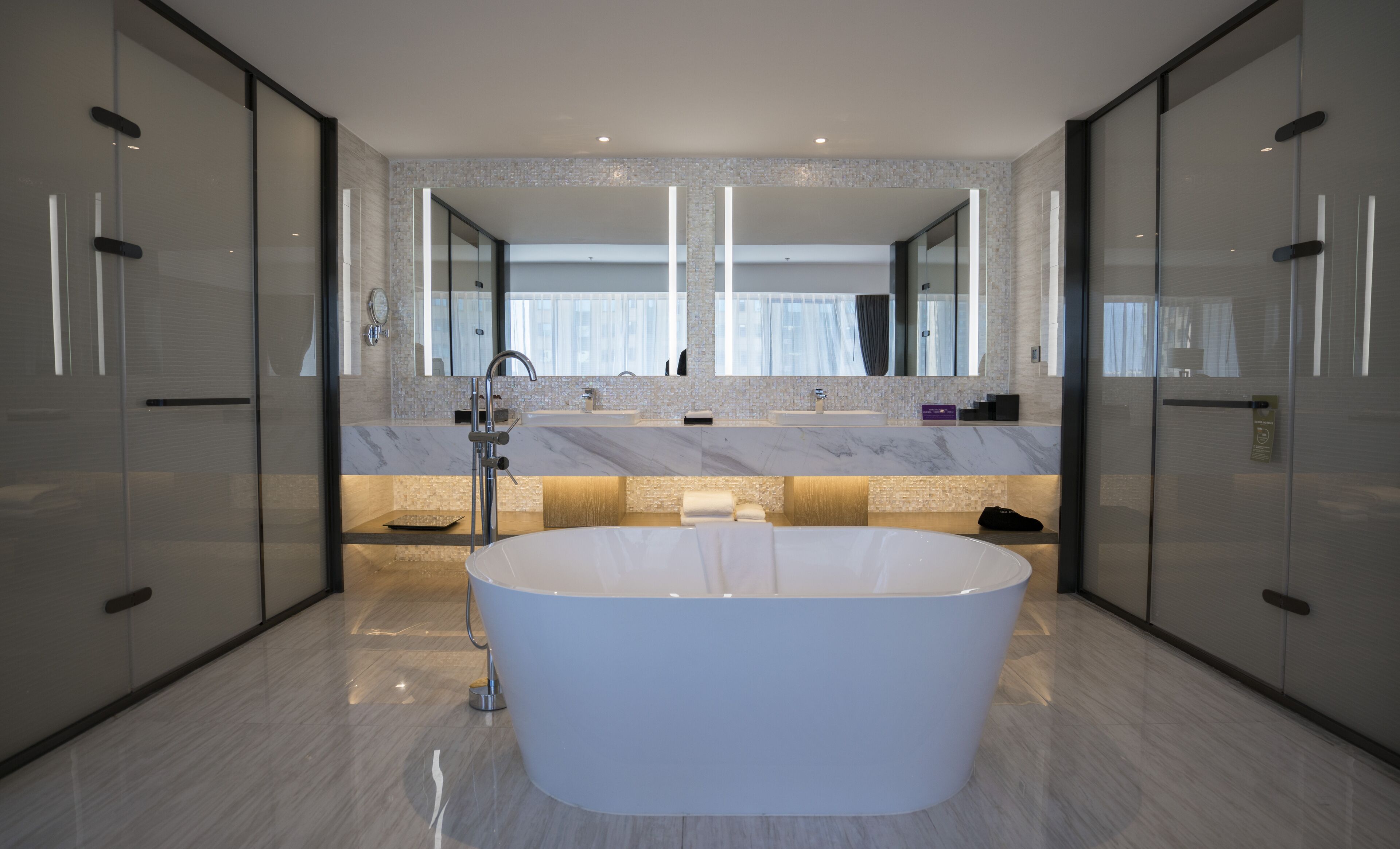 A modern bathroom with a freestanding bathtub, two sinks, and a large mirror.