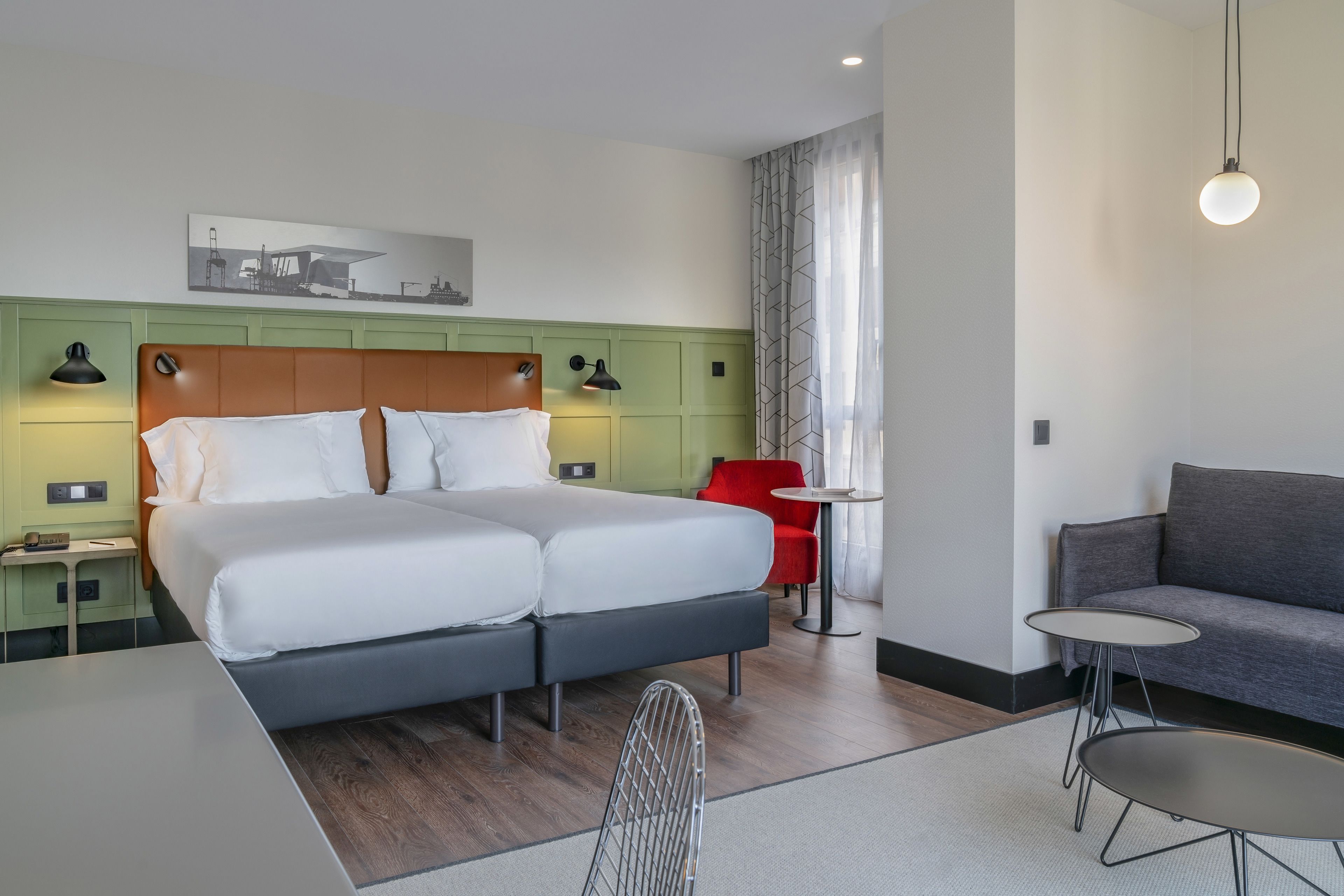Quarto de hotel com cama de casal, escrivaninha, cadeira, sofá e mesa pequena.