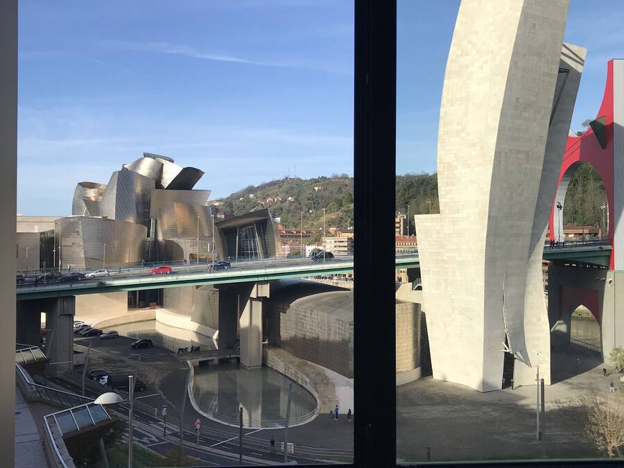 A view of a modern architectural structure with a large, curved concrete pillar and a bridge overhead.