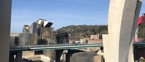A modern architectural structure with a curved concrete pillar and a bridge with pedestrians.