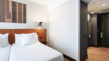 A modern hotel room with a large bed, a headboard, a wall-mounted artwork, and a door leading to a bathroom.