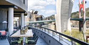 Un espace extérieur aménagé avec une table et des chaises, offrant une vue sur une rivière et un pont.