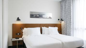 Una habitación de hotel con una cama doble, una mesita de noche con un teléfono, una lámpara de pared y un cuadro de estructuras industriales.