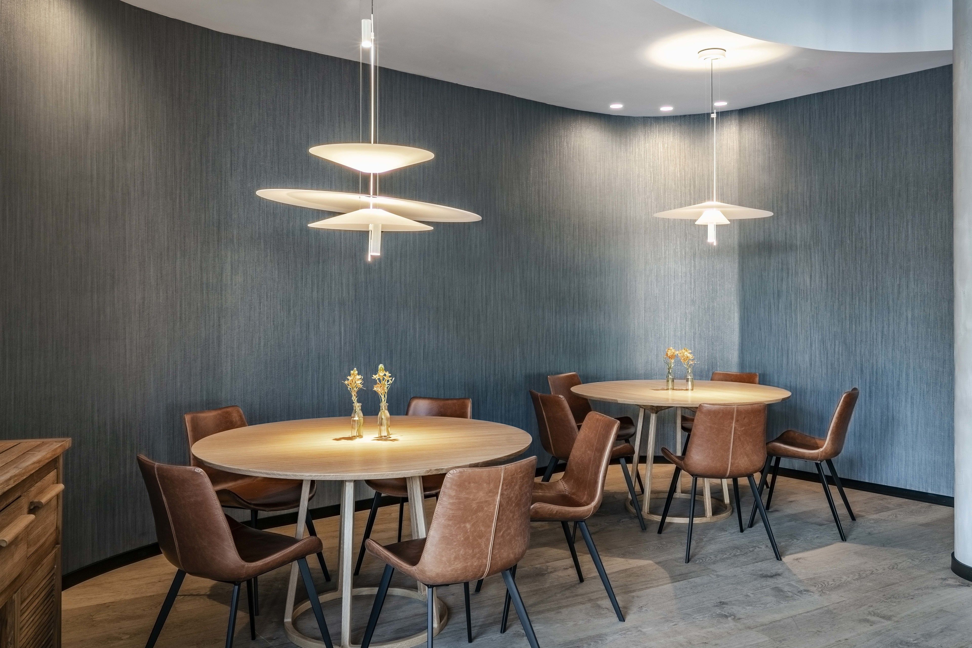 A modern dining area with round tables and brown leather chairs, featuring pendant lighting and a textured wall.