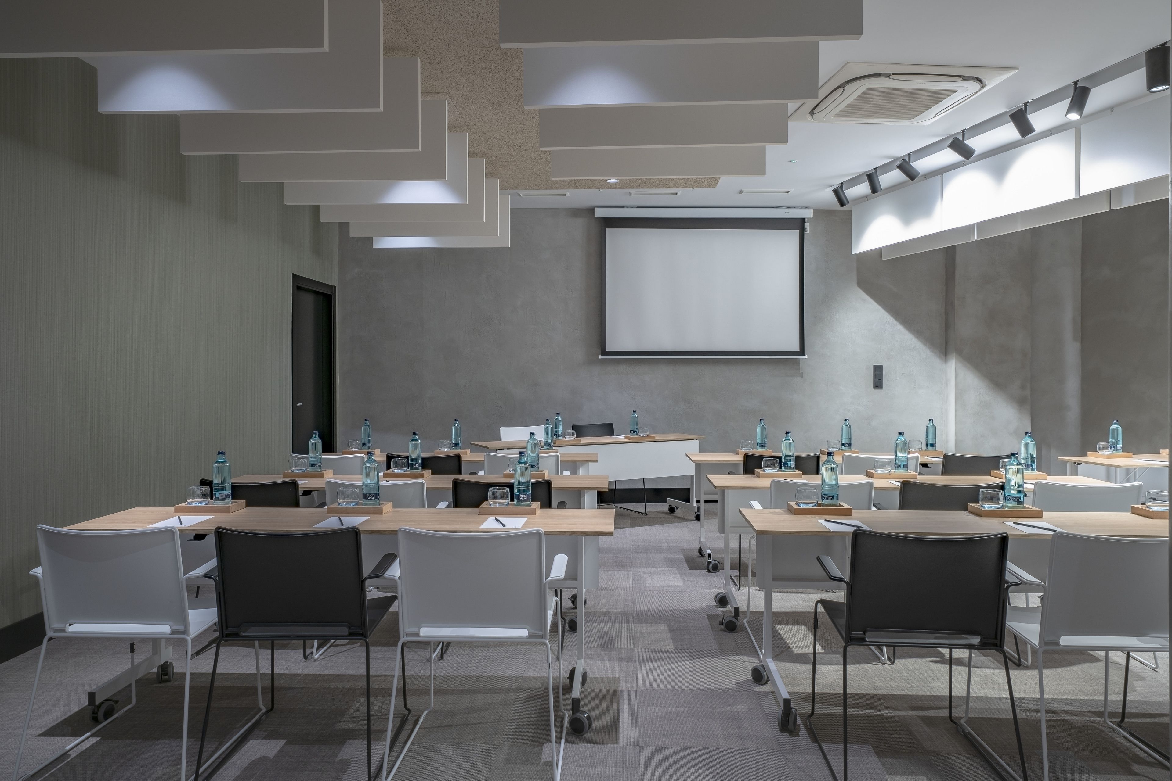 Un salón de conferencias con varias mesas y sillas, equipado con botellas de agua y ordenadores portátiles.