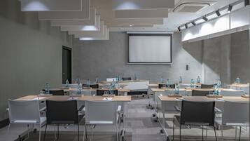 Un salón de conferencias con varias mesas y sillas, equipado con botellas de agua y ordenadores portátiles.