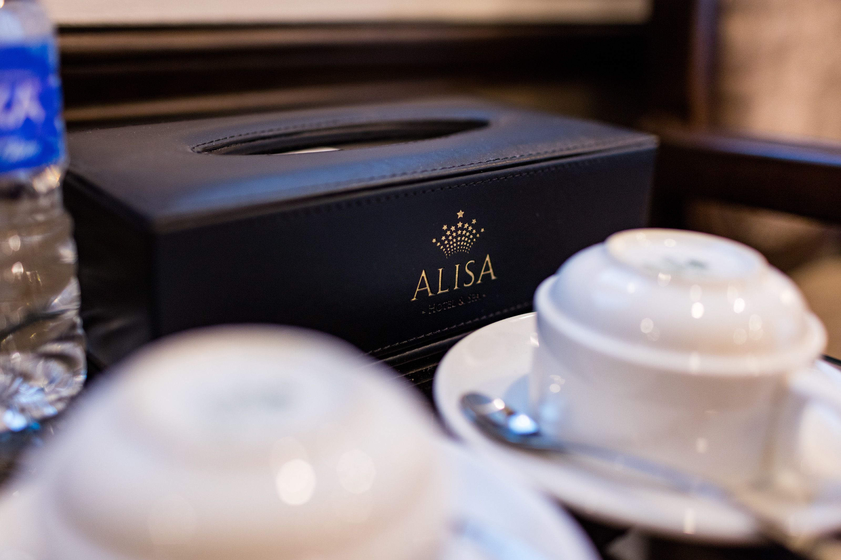 A black tissue box with the brand name 'ALISA' on a table with a white cup and saucer.