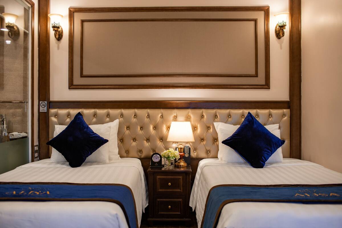 A hotel room with two beds, a large padded headboard, bedside lamps, a nightstand with a clock, and a mirror.