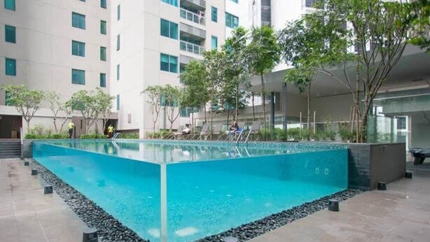 A rectangular pool with clear blue water, surrounded by a pebble border, and adjacent to a modern building with multiple windows and balconies. - Mercu Summer Suite KLCC by Fervent (Kuala Lumpur)