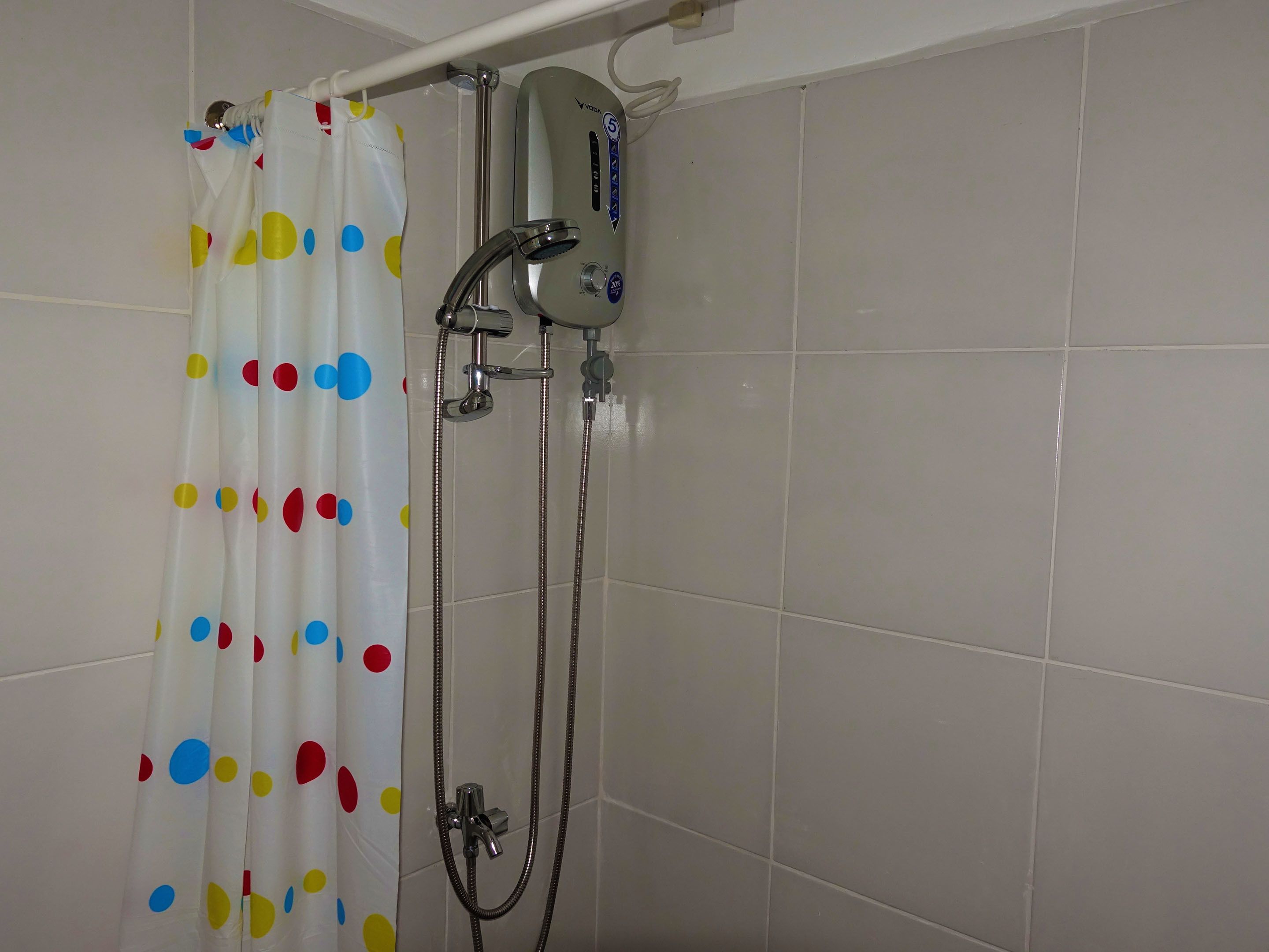 Un espace douche doté d’un rideau de douche à pois, d’un pommeau de douche à main et d’un chauffe-eau mural.