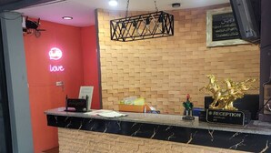 Un comptoir d’accueil avec un plateau en marbre, un néon en forme de cœur, un mur décoré d’un motif en briques et un téléviseur fixé au mur.