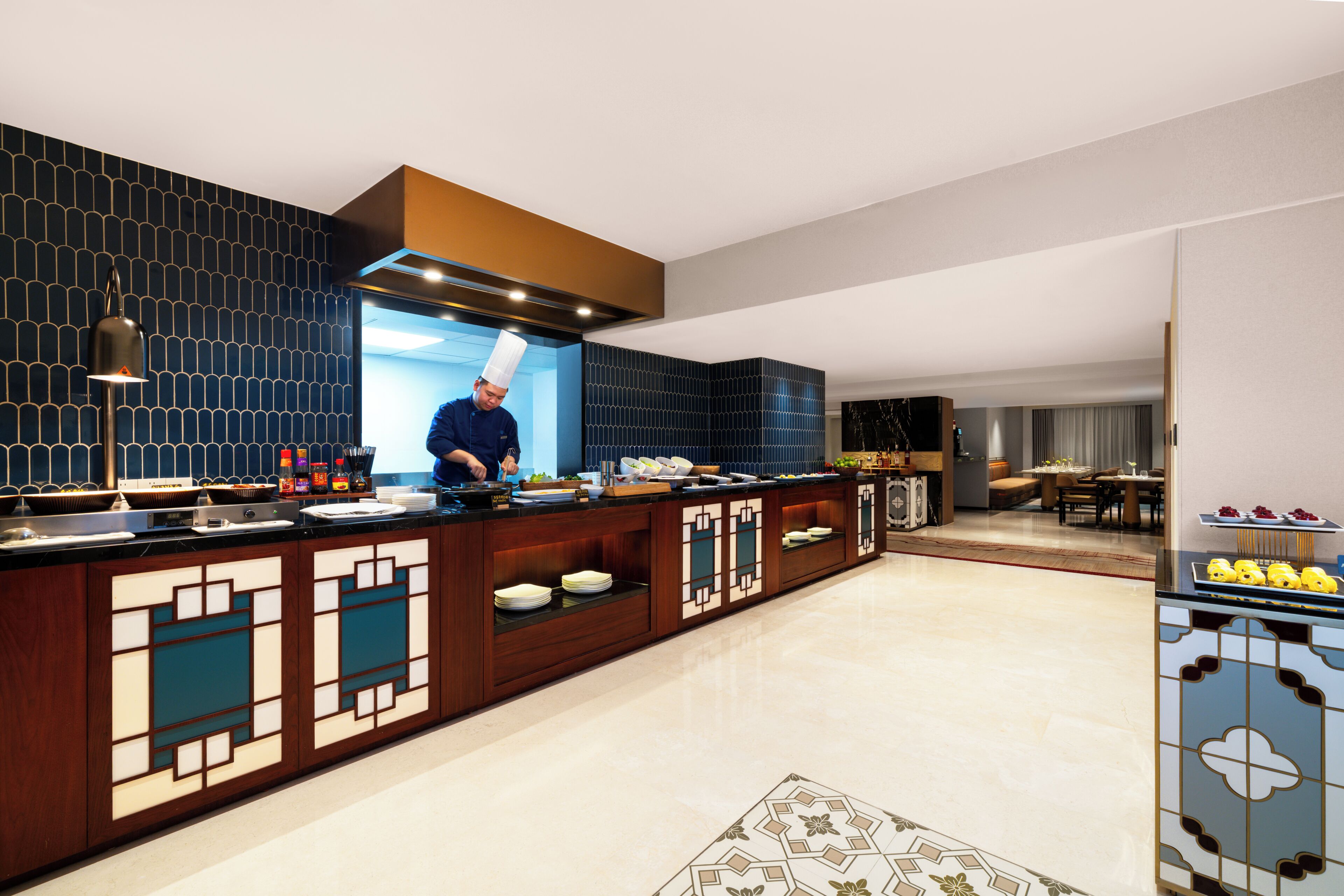 Una cocina moderna con un chef preparando comida, un comedor con mesa y sillas, y un bufé con diversos platos.