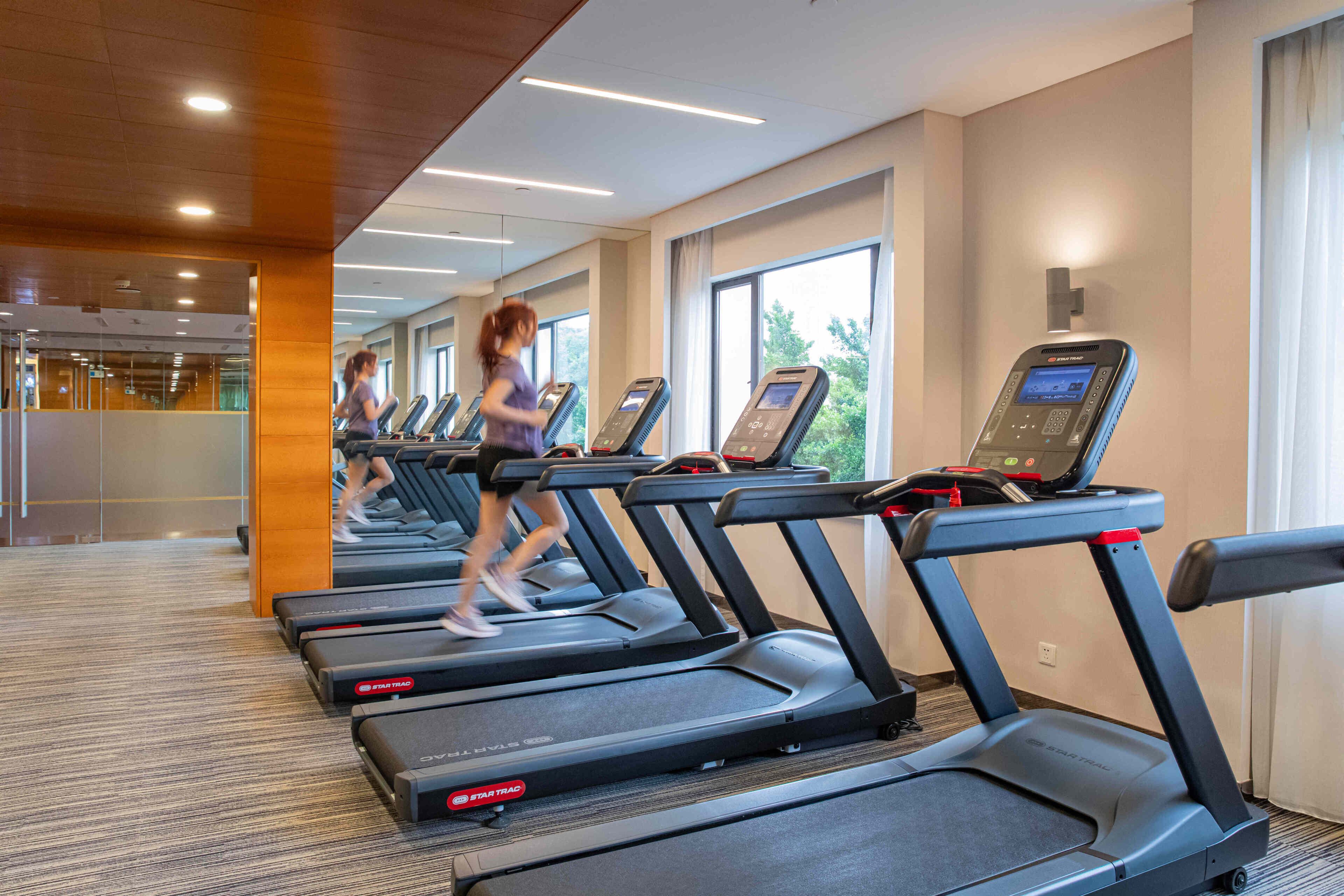A gym with treadmills, a mirror, and large windows.