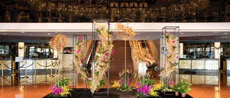 A lobby with a modern design, featuring a central floral display and a ceiling with intricate light patterns.