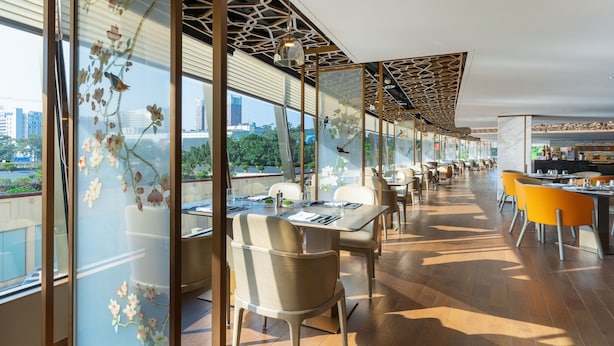 A modern restaurant with a long dining area, large windows, and a view of the cityscape. - China Hotel (Guangzhou)