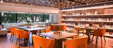 A modern library with wooden floors, orange chairs, and bookshelves.