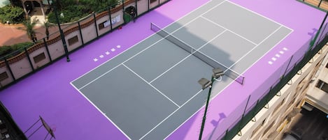 An outdoor tennis court with a purple surface, surrounded by a fence and greenery.