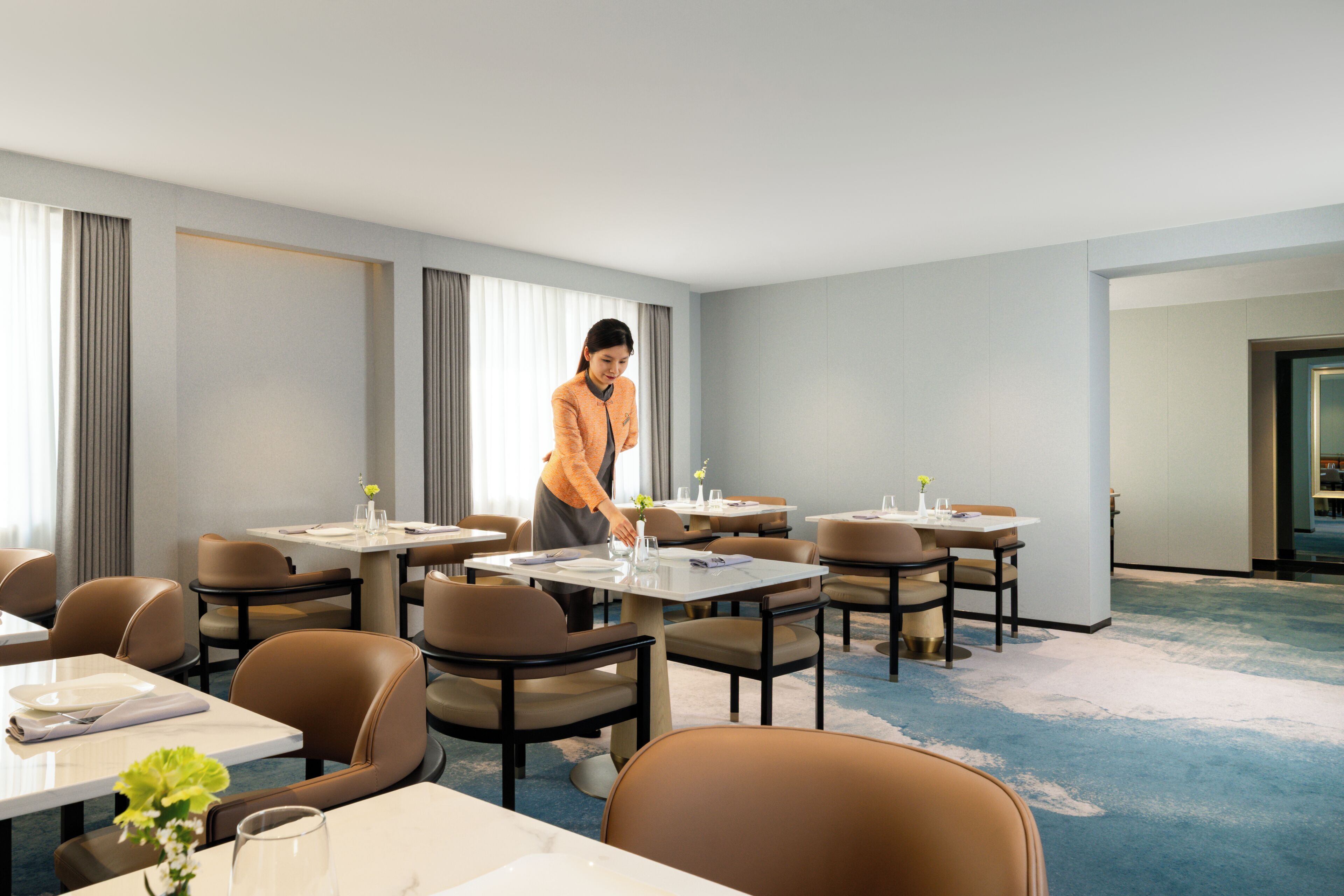 A hotel room with multiple tables and chairs, a carpeted floor, and a large window with curtains.