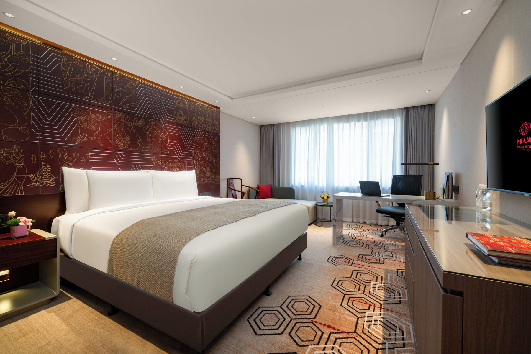 A modern hotel room with a large bed, a desk with a computer, a TV, and a decorative wall.