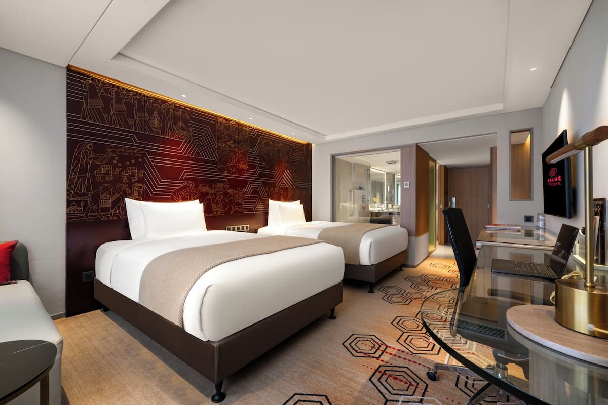 Ein modernes Hotelzimmer mit zwei Betten, einem Schreibtisch und einem Fernseher.