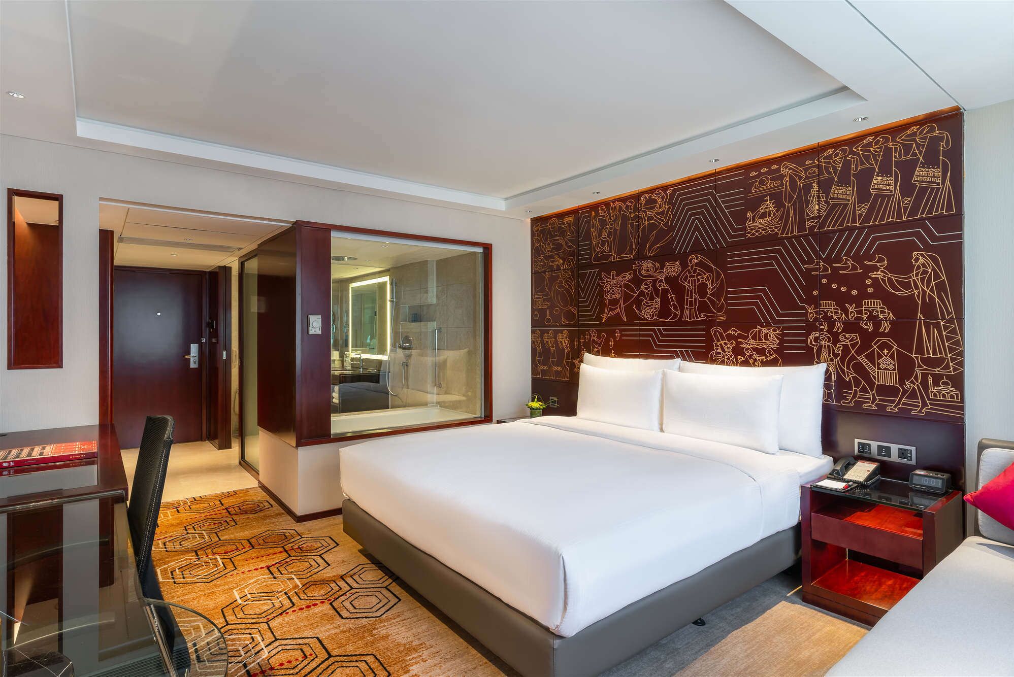 Une chambre d’hôtel dotée d’un grand lit, d’un bureau, d’une chaise, d’une douche en verre et d’un mur décoratif orné de motifs.