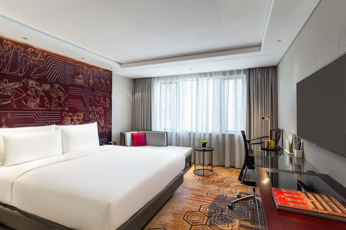 Ein Hotelzimmer mit einem großen Bett, einem Schreibtisch mit Stuhl, einem Fernseher und einem Fenster mit Vorhängen.