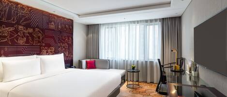 Habitación de hotel con una cama grande, un escritorio con silla, televisión y ventana con cortinas.