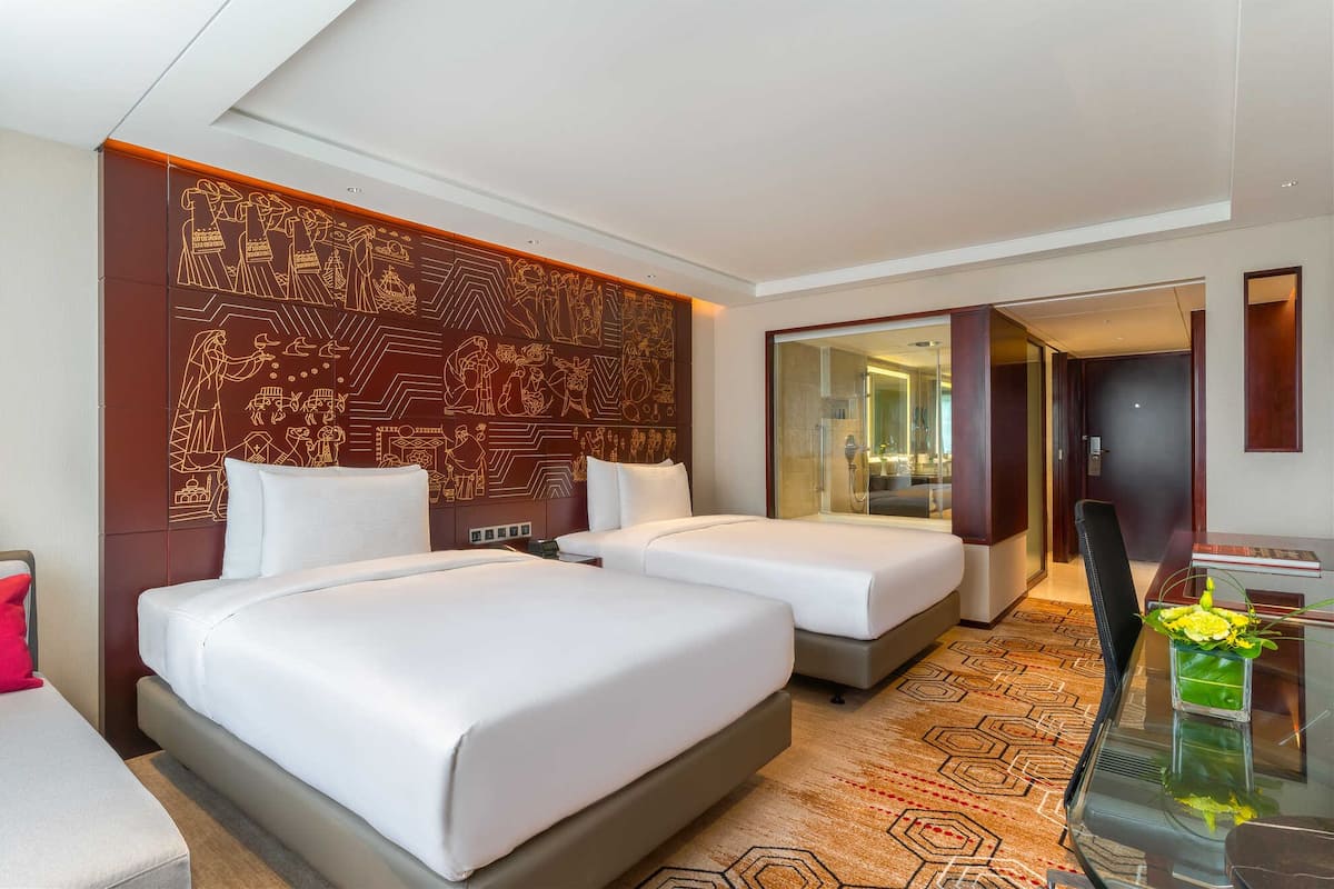 Ein Hotelzimmer mit zwei Betten, einem Glastisch, einem Fernseher und einer Wanddekoration.