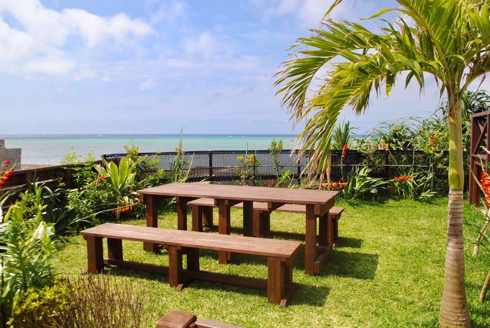 A wooden picnic table and bench set on a grassy lawn with a view of the ocean.