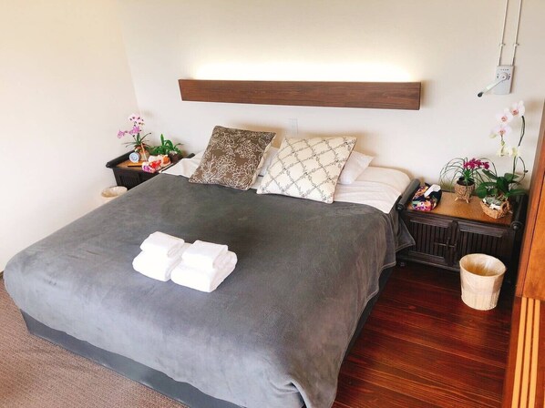 A neatly made bed with a grey bedspread, two pillows, and a set of white towels.