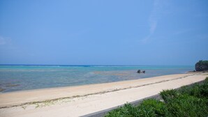 A beach with clear blue water, a sandy shore, and some greenery in the foreground. - Shirahama no yado shiokaze (Nakijin)