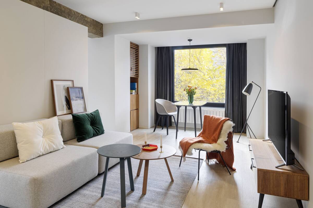 A modern living room with a sofa, a coffee table, a chair, a TV, and a dining area with a table and chairs.