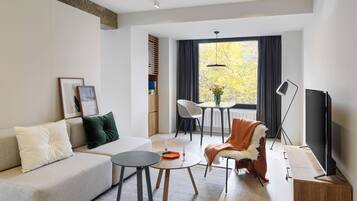 A modern living room with a sofa, a coffee table, a chair, a TV, and a dining area with a table and chairs.
