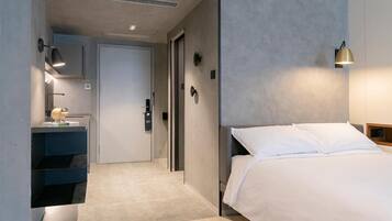 Habitación de hotel moderna con cama, mesita de noche, lámpara, espejo, puerta y un pequeño estante con un adorno.