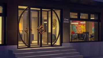 A modern building entrance with glass doors, a staircase, and a colorful interior visible through the windows.