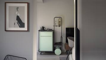 Una habitación minimalista con una obra de arte enmarcada, un carrito verde con un hervidor y una silla.