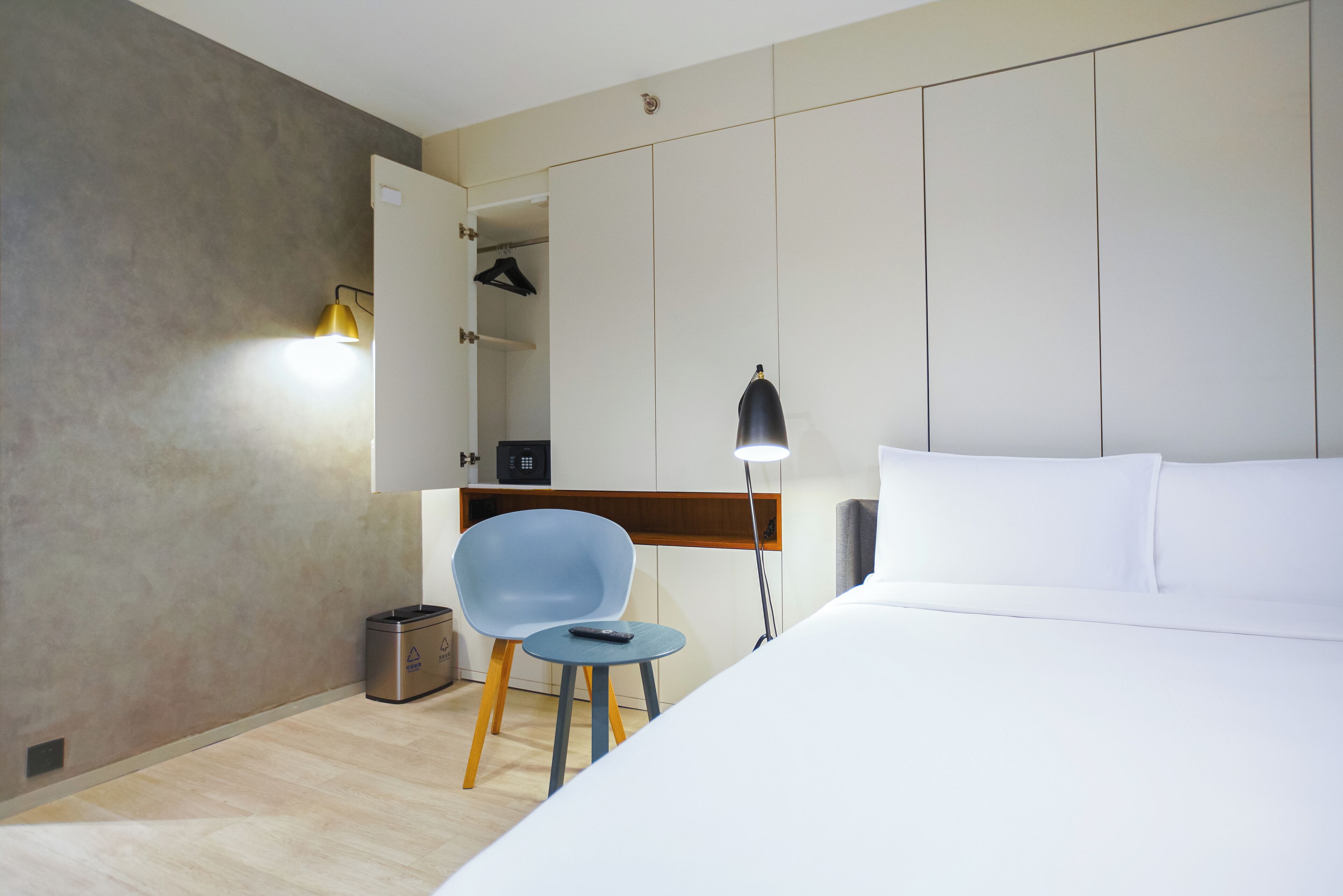 A hotel room with a bed, a chair, a desk, a lamp, and a wardrobe.